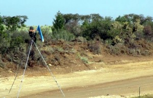 A person ensures stoppage of vehicle traffic by perching their own body atop a tripod, a part of a range of blockade tactics shutting down work at the site today. 